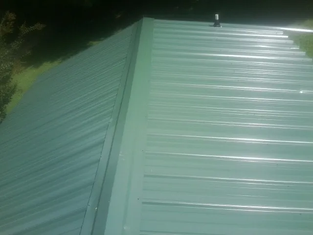 New green metal panels meeting at the ridge of a roof — Flat Roof Repair work by our crew in Ionia