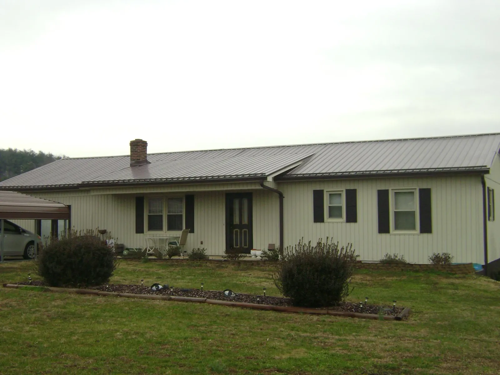 Brown metal roof on a cream sided ranch home with a brick chimney in Ionia